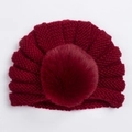 Texture tricotée détaillée d'un bonnet bébé rouge foncé avec un grand pompon en fausse fourrure - Bordeaux
