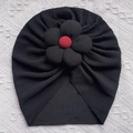 Detail einer schwarzen Turbanmütze für Babys mit großer Blume und rotem Zierknopf - Schwarz