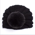 Gros plan détaillé d'un bonnet turban tricoté noir pour bébé avec un grand pompon en fourrure - Noir