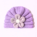 Detail der Baby-Strickmütze mit lavendelfarbenem Wellenmuster und großer Blumenverzierung - Lila