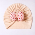 Pink knit baby turban hat featuring a large white bow with red polka dots design - Nude Pink