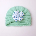 Soft mint green knitted baby hat featuring a large blue polka dot fabric flower decoration - Mint Green