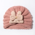Close-up of pink knitted baby hat with cute beige rabbit doll and a large bow decor - Coffee