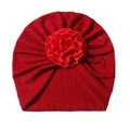 Detail of red knitted baby turban cap featuring a large satin rose and textured pleats - Red