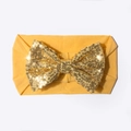 Vue détaillée du bandeau bébé gingembre avec un avec grand nœud doré à paillettes brillantes - Jaune