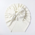 Detail showing the ribbed knit texture and large bow on this soft white baby turban hat - Beige