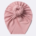 Detail einer rosa gestrickten Baby-Mütze mit Donut-Knoten auf weißem Hintergrund - Nute Rosa