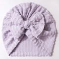 Detailaufnahme der fliederfarbenen Baby-Mütze mit Jacquard-Struktur und großer Schleife - Lila