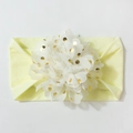 Détail d'un bandeau bébé avec de grandes fleurs blanches et des pois dorés brillants - Beige