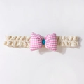 Detail eines Baby-Spitzenstirnbands mit rosa karierter Schleife auf weißem Hintergrund - Rosa
