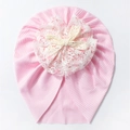 Close-up of pink ribbed baby beanie with large white lace flower and crochet bow detail - Pink