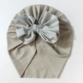 Detail of baby ribbed knit turban featuring a large soft grey satin bow on beige fabric - Gray