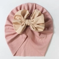 Close-up of baby turban hat featuring a champagne bow on dusty pink ribbed fabric - Nude Pink
