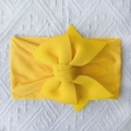 Detail of soft yellow nylon baby headband with large double-layered bow on white knit - Bright Yellow