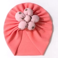 Infant turban hat in coral pink with a large polka dot fabric flower on white background - Pink