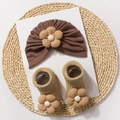 Detail of warm baby hat and socks set with 3D floral ornaments on a natural straw mat - Coffee