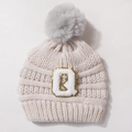 Detail of knitted beige baby hat with soft grey pom-pom and letter Q patch embroidery - Beige + Gray