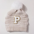 Detailed close-up of beige knit baby hat with white pompom and sparkling letter P patch - Beige