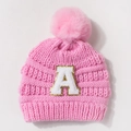 Detail of pink knitted baby hat featuring large faux fur pompom and chenille letter A patch - Pink