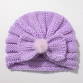 Detailed texture of lavender knitted baby hat with a large bow and pink faux fur pompom - Purple