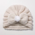 Detail of a beige knit baby turban hat featuring a large soft bow and faux fur pompom - White