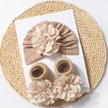Detail of baby knitted hat and ribbed socks set with 3D flower decor on white card - Coffee