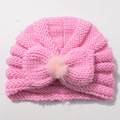 Detail showing pink knit baby hat with ribbed texture and decorative bow with faux fur pom - Pink