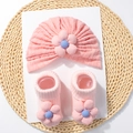 Detailed view of pink knitted baby turban hat and matching flower socks on a straw mat - Snow Bud