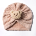 Detail view of a soft pink plush baby hat featuring a cute teddy bear and knotted top - Nude Pink