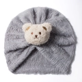Detail of dark grey plush baby turban hat featuring a cute teddy bear patch on white background - Gray