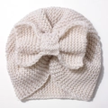 Detailed close-up of cream knit baby turban hat featuring a large soft bow decoration - Beige