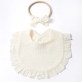 Detail view of cream cotton bib with ruffle edges and matching bow headband set for infants - Beige