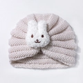 Detailed close-up of soft beige knit texture and cute plush bunny face on a baby winter hat - Beige