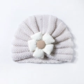 Detailed view of cream baby knitted turban hat with white floral ornament and brown center - Beige