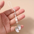Close-up of white enamel paw pendant and beaded strap held in hand for phone accessory detail - White