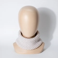 Detalle del tejido de punto de un cuello beige para bebé sobre un soporte de madera - Beige