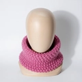 Detalle de calentador de cuello rosa para bebé en punto grueso con textura sobre busto madera - Rosa Palo