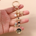 Detalle de llavero náutico dorado con estrella de mar, pez y colgante de coral grabado - Gold Black Round Tree of Life