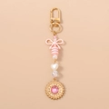Detalle de llavero con lazo rosa, cuentas de corazón y colgante de sol dorado con cristal - Estilo Sol con Lazo de Perlas