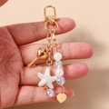 Dettaglio del portachiavi con perline, chiave a cuore e stella marina in mano - Stella Marina Chiave Perlinato Cuore (Oro)