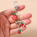 Detail of a strawberry metal keychain with 3D resin fruit and charms held by hand - Square Strawberry