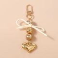 Close-up of golden beaded keychain featuring a white bow and a polished heart pendant - Gold