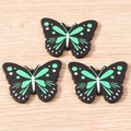 Detailed macro view of three butterfly charms with green patterns on a wooden surface - 10 Pieces Pack / Green