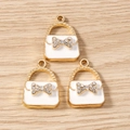 Detailed close-up of three handbag-shaped alloy pendants with enamel and bow rhinestones - White