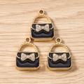 Close-up of golden handbag charms with black enamel finish and rhinestone bow details - Black