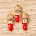 Macro-opname van drie gouden lippenstift-hangers met kleurrijke strass-steentjes op hout - 10 Stuks Verpakking / Rood