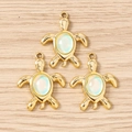 Detailed macro view of three golden turtle pendants with opal inlay on a wooden background - 10 Pieces Pack / Gold Green