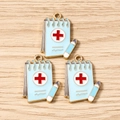 Detailed macro of medical notepad charms with red cross and pen for jewelry DIY - Blue