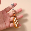 Detail of realistic bread keychain held in hand showing beads and silver metal clasp - Bread