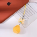 Vista detallada del colgante amarillo con lazo y cesta fijado a un smartphone naranja - Amarillo